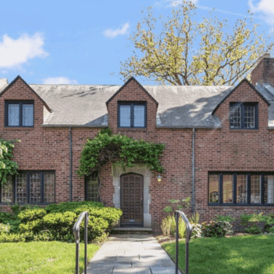 Charming brick house with dormer windows and a lush green front yard.