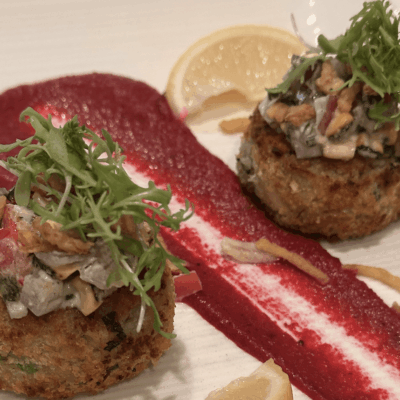 Two gourmet crab cakes garnished with greens and sauce.