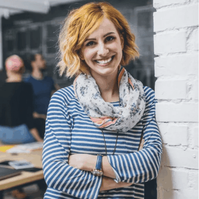 Smiling woman with arms crossed wearing a striped shirt and floral scarf.