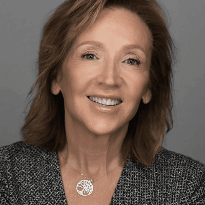 Smiling middle-aged woman with light brown hair against a gray background.