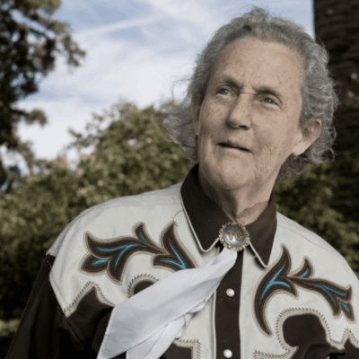 An older man in a western-style shirt outdoors holding white flowers.