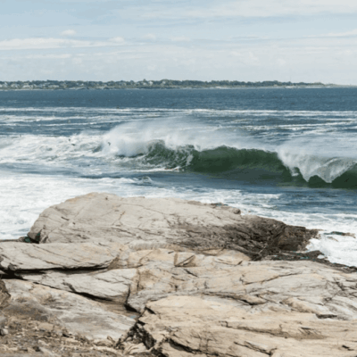 Waves crashing on rocky shoreline under partly cloudy sky.
