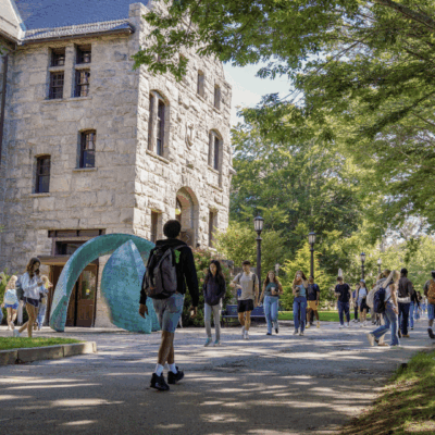 College students walking near a historic campus building with a tent set up outside.