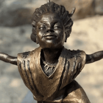 Bronze sculpture of a joyful child with outstretched arms.