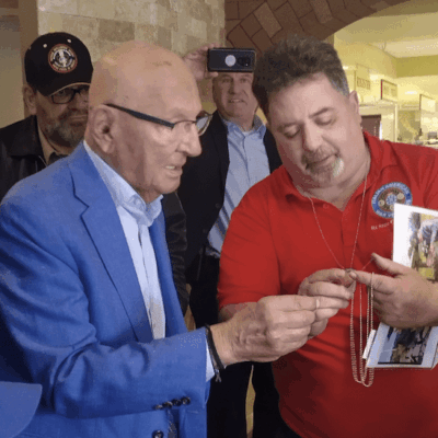 Elderly man in blue suit signing autographs for fans in a crowd.