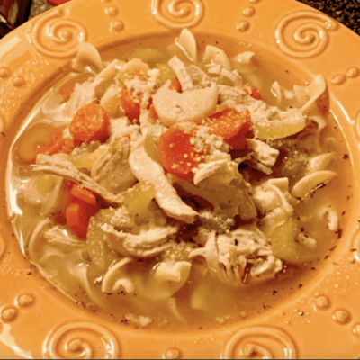 A bowl of chicken noodle soup with vegetables on a decorative plate.
