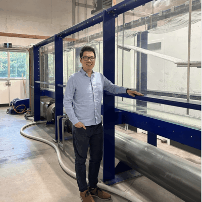 Man in business casual attire stands next to industrial equipment indoors.