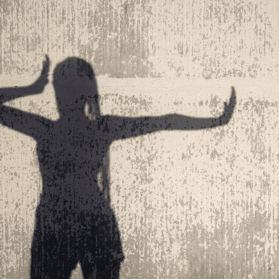 Shadow of a person with hands raised against a textured wall.