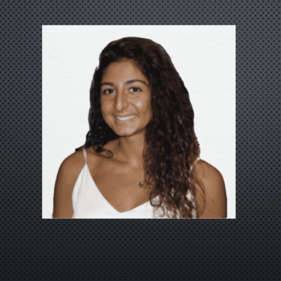 Young woman with curly hair smiling at the camera against a plain background.