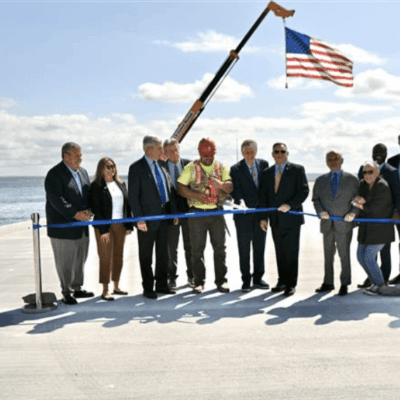 Group cutting ribbon at outdoor ceremony with American flag.