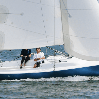 Two men sailing on a small sailboat with white sails on calm water.