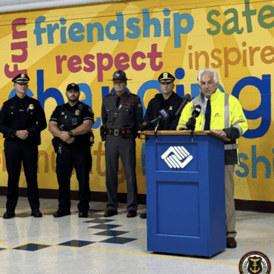 Police officers and a speaker at a podium in a school hallway decorated with positive words.