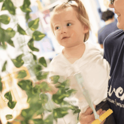 A toddler girl looking curiously at plants while holding a white flower.