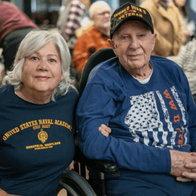 An elderly couple sitting together wearing patriotic-themed shirts.