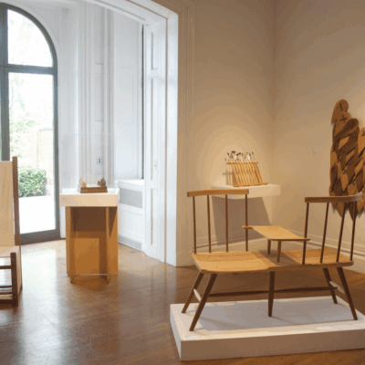 Minimalist chairs displayed in a sunlit gallery room with wooden floors.