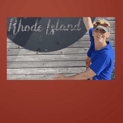 A man in sunglasses and a cap pointing at a Rhode Island sign.