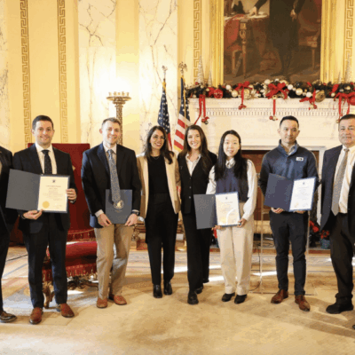 Group of six people posing with certificates and awards indoors.