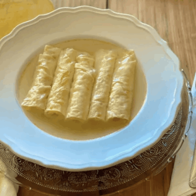 Five cannelloni pasta rolls in creamy sauce on a white plate.