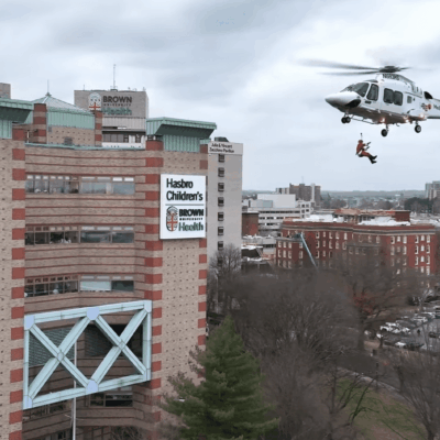 Medical helicopter flying near a hospital building on a cloudy day.