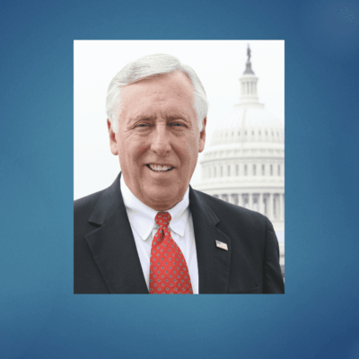 Portrait of a smiling elderly man in a suit with the U.S. Capitol in the background.
