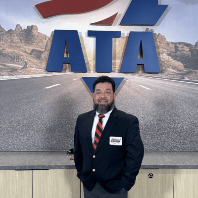 Man in business suit stands in front of large ATA logo indoors.