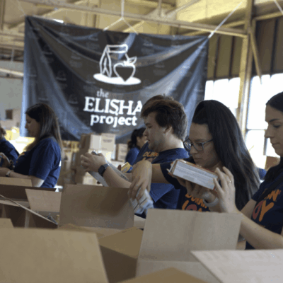 Volunteers packing boxes at a community aid event under a project banner.