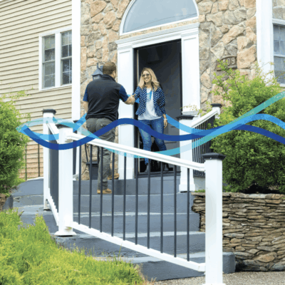 Two women greeting each other on a front porch with a blue ribbon decoration.