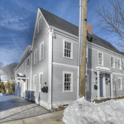A large gray house with white trim on a snowy day under a clear blue sky.