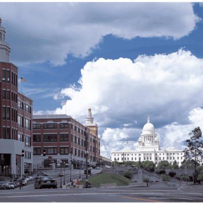 View of a city street leading to a domed government building under a cloudy sky.
