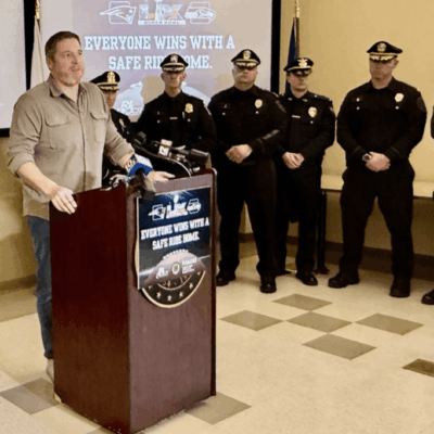Police officers and a man stand at a podium during a public safety event.