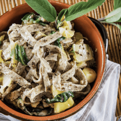A bowl of creamy pasta with fresh herbs and zucchini.