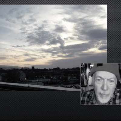 Sunset with cloudy sky over a cityscape, video call window with a man's face.