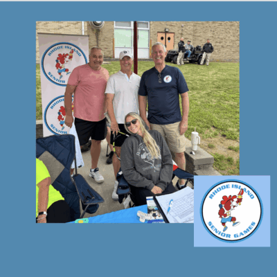 Four people smiling at an outdoor event booth with a mascot logo.