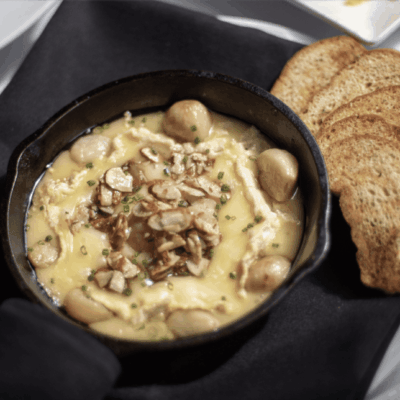 Baked cheese dip topped with nuts served with toasted bread slices.