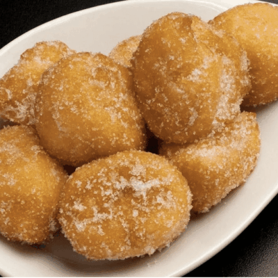 Sugary fried doughnuts piled on a white plate.