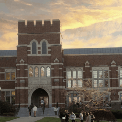 Historic brick university building at sunset with people gathered outside.