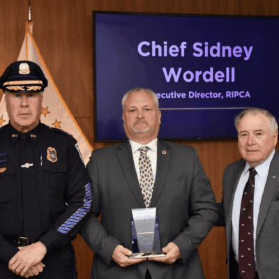 Chief Sidney Wordell stands with two men, one holding an award plaque.