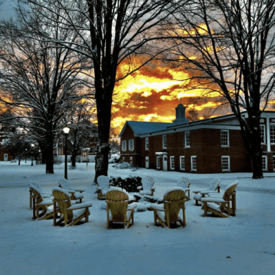 Snow-covered courtyard with fire pit chairs at sunset.
