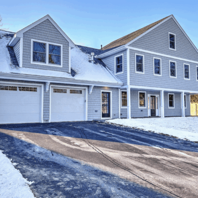 Modern gray house with snow-covered roof and driveway.