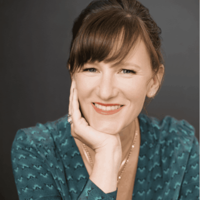 Smiling woman resting her chin on her hand, wearing a teal patterned shirt.