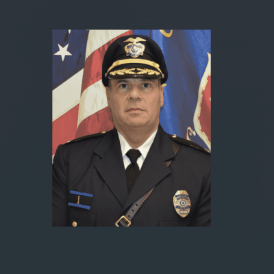 Portrait of a uniformed police officer with flags in the background.