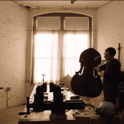 Man crafting a double bass in his workshop.