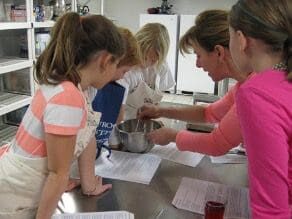 A group of children are mixing ingredients in a kitchen.