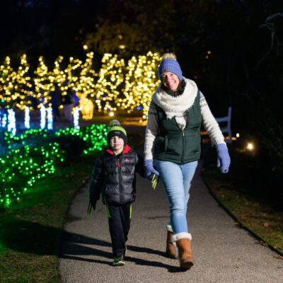 A woman and child walking together on a lit path at night.