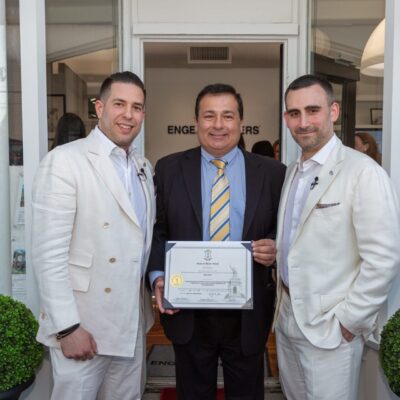Three men in suits holding a certificate in front of a store.
