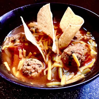 A bowl of soup with meatballs and tortillas.