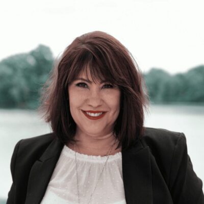A woman smiling in front of a lake.