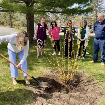 Woman planting tree with group observing nearby.