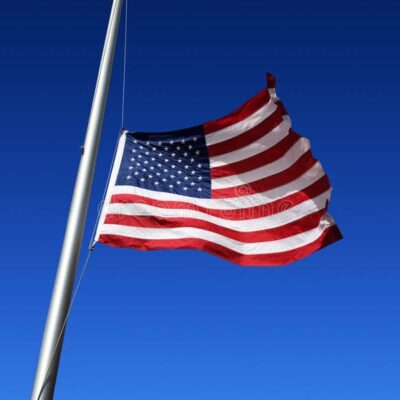 An american flag flies in the wind against a blue sky.