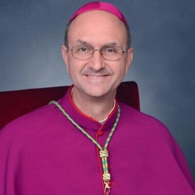 Man in bishop attire with glasses smiling.